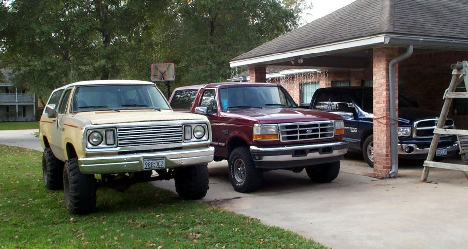 1978 Dodge Power Ram lifted with large tires, parked next to a maroon Ford Bronco and a dark blue Dodge Ram pickup