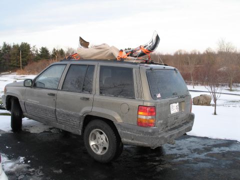 1995 Ford Bronco - A Jeep Grand Cherokee with a kayak secured to its roof rack sits parked on a wet, snowy surface.
