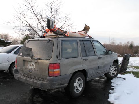 1995 Ford Bronco - A gray Jeep Grand Cherokee is parked next to another vehicle, with items strapped to its roof rack.