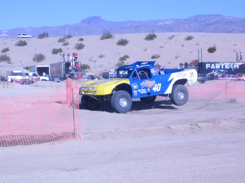 Number 40 blue and yellow race truck on a banked dirt corner in the desert