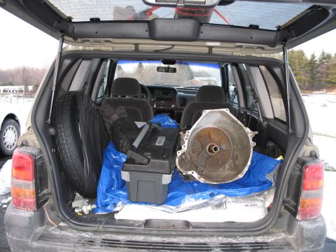 1995 Ford Bronco - The rear cargo area of an SUV is filled with various items, including a spare tire and a large transmission component.