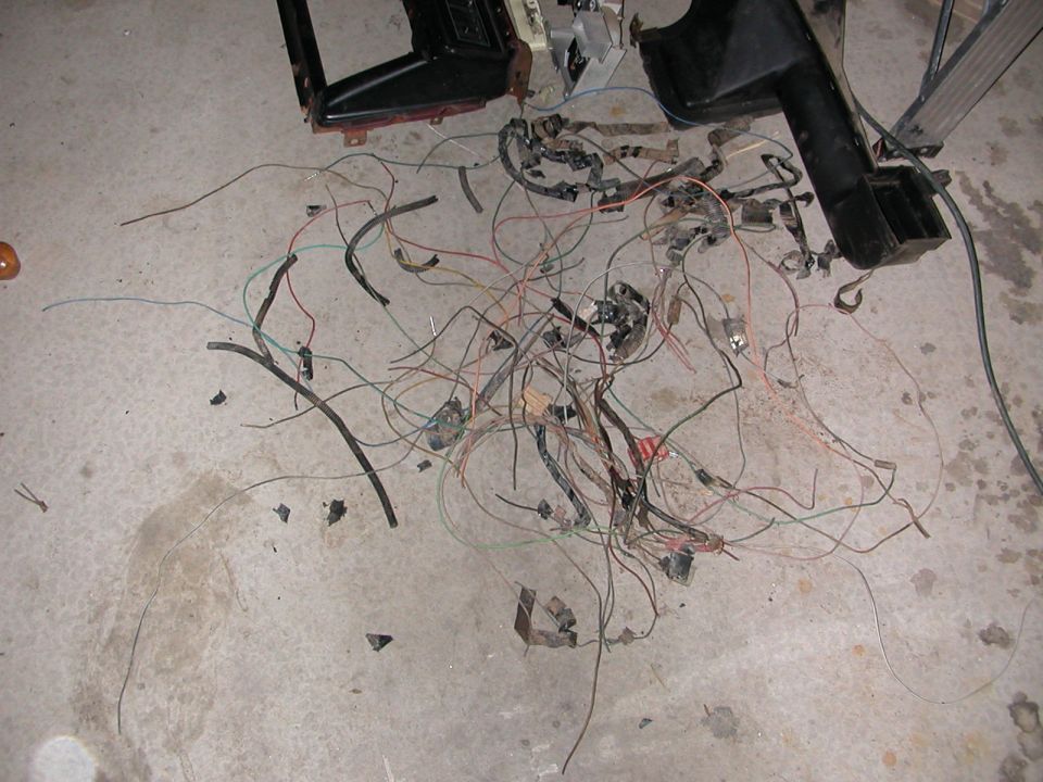 Tangled mess of wires and connectors on a concrete floor, with some black plastic dashboard pieces nearby
