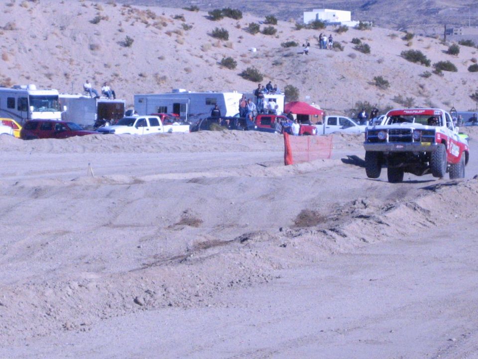 Red and white race truck cornering on a desert dirt course with spectators