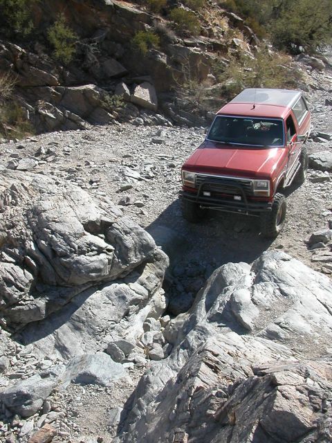1984 Ford Bronco - A red SUV tackles a challenging rocky terrain on an off-road trail.