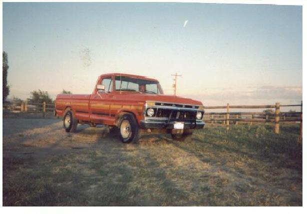 Red Ford pickup truck parked on dirt lot by a wooden fence at dusk.