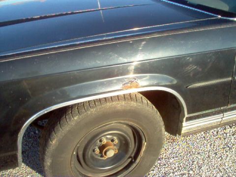 1985 Ford LTD Crown Victoria - Close-up of a dark-colored car's front fender and wheel, showing signs of wear and rust.