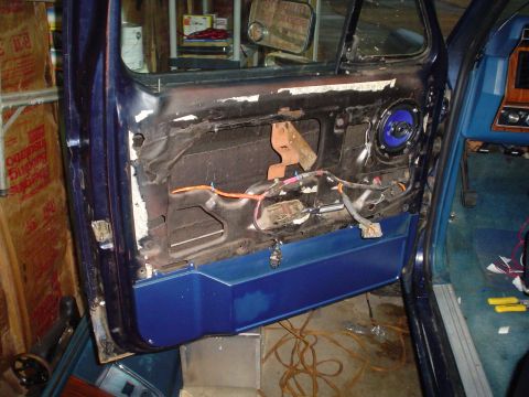 1984 Ford Bronco - The interior of a vehicle door with the panel removed, revealing wiring and a speaker. The blue door panel is partially visible.