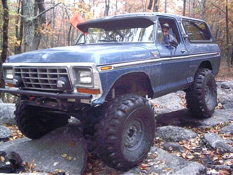 1993 Ford Bronco - This modified Ford Bronco is shown off-roading over rocks in a wooded area.