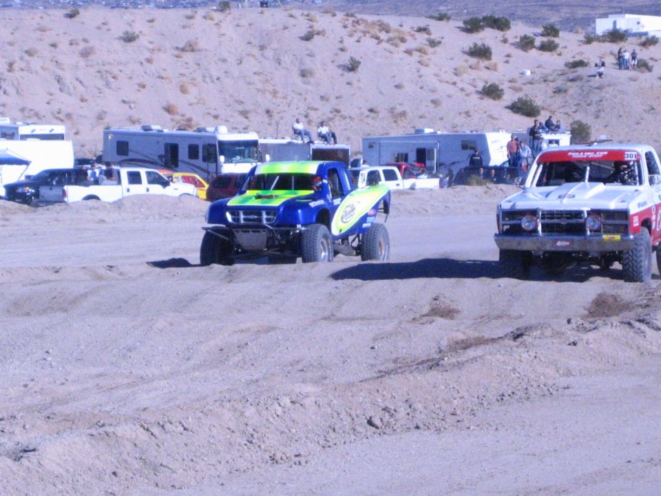 Green and blue race truck and red-white truck side by side on dirt track