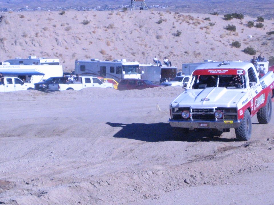 Red and white number 308 off-road race truck cornering on a desert dirt track