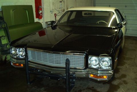 1991 Ford Crown Victoria - This black and white sedan, possibly a police car, is parked indoors with a large green car hood nearby.