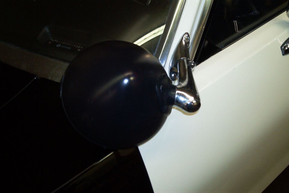 Close-up of a black ball-shaped spotlight mounted at the A-pillar of a white-and-dark car