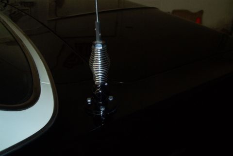 1991 Ford LTD Crown Victoria - Close-up of a chrome spring-base whip antenna mounted on the dark rear trunk lid of a two-tone car.
