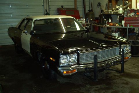1991 Ford LTD Crown Victoria - Black-and-white two-tone full-size sedan with roof light bar and push bumper parked inside a workshop garage.