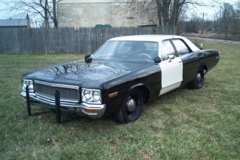 1991 Ford LTD Crown Victoria - Black-and-white two-tone vintage full-size sedan with push bumper parked on grass before a wood fence and railroad track.