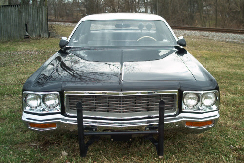 Front view of a dark full-size sedan with chrome grille and black push bumper on grass