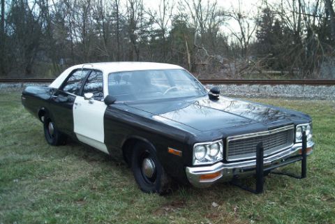 1991 Ford LTD Crown Victoria - Black-and-white two-tone full-size police sedan with white roof and push bumper parked on grass near bare winter trees.