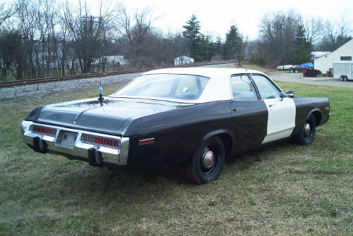 Rear three-quarter view of a black-and-white full-size police sedan parked on grass