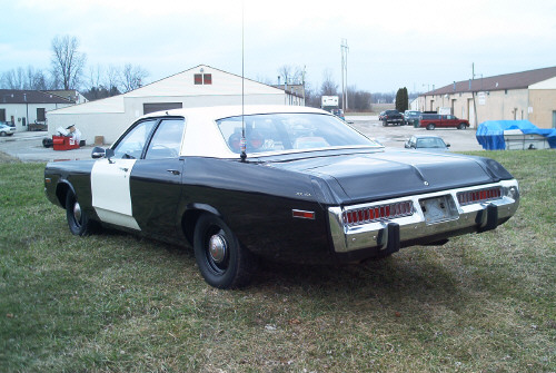 Rear three-quarter view of a black-and-white police sedan in a paved lot near buildings