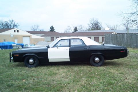 1991 Ford LTD Crown Victoria - Side profile of a black-and-white two-tone full-size sedan with white roof parked on grass near storage buildings.