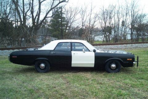 1991 Ford LTD Crown Victoria - Side profile of a black-and-white two-tone full-size sedan with push bumper parked on grass by a railroad track and bare trees.