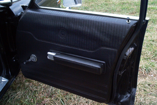 Interior door panel of a dark car with chrome handle, lock, and window crank