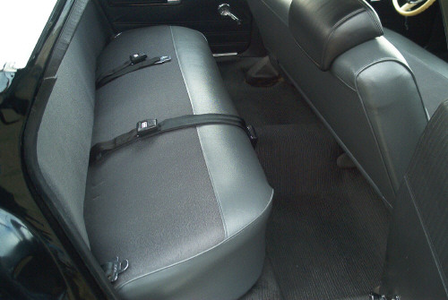 Rear bench seat in gray and black vinyl with lap belts inside a dark car