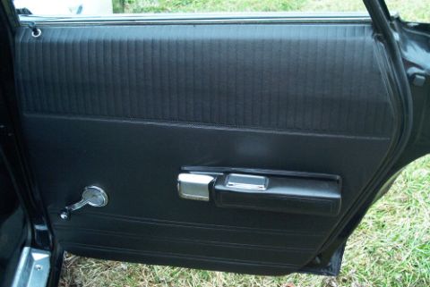 1991 Ford LTD Crown Victoria - Black interior door panel showing a chrome door handle, armrest pull, and lock, with the door opened over grass.