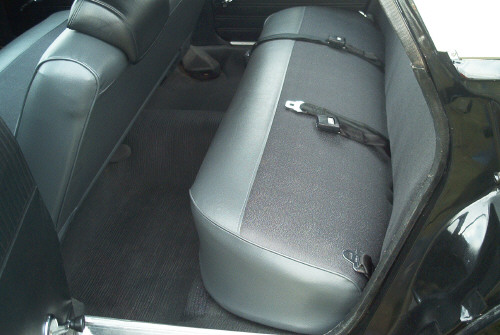 Rear bench seat in gray and black vinyl with seat belt in a dark car