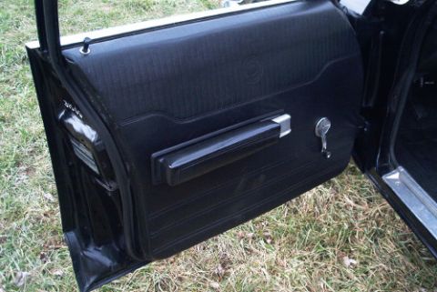 1991 Ford LTD Crown Victoria - Black vinyl interior door panel with chrome handle, armrest, and a visible side mirror, door open over grass.