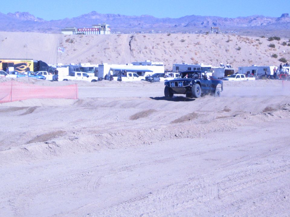 Dark off-road race truck raising dust on a desert track