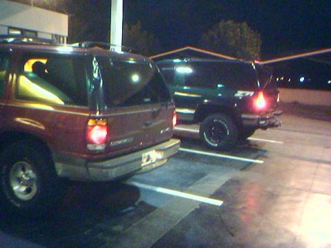 1996 Ford Explorer - Two SUVs are parked side-by-side in a lot at night, with one in the foreground and another behind it.