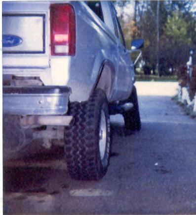1989 Ford Bronco - Rear view of a silver Ford truck with a prominent off-road tire and chrome bumper.