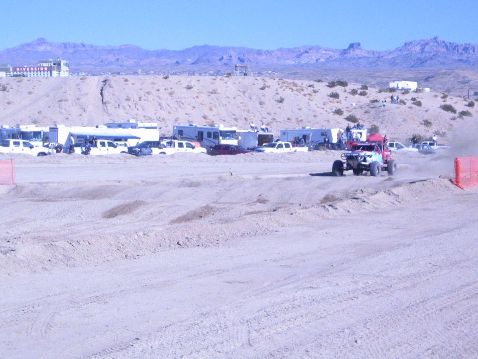 Red off-road race truck raising dust on a wide desert course