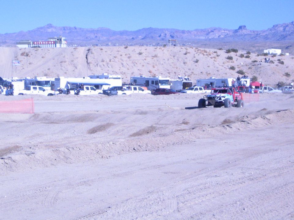 Off-road race buggy on a sandy desert course with RVs and mountains behind