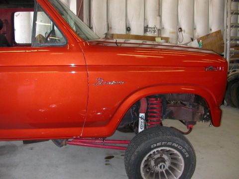 1984 Ford Bronco - Orange Ford Bronco with custom red suspension and visible fender badge.