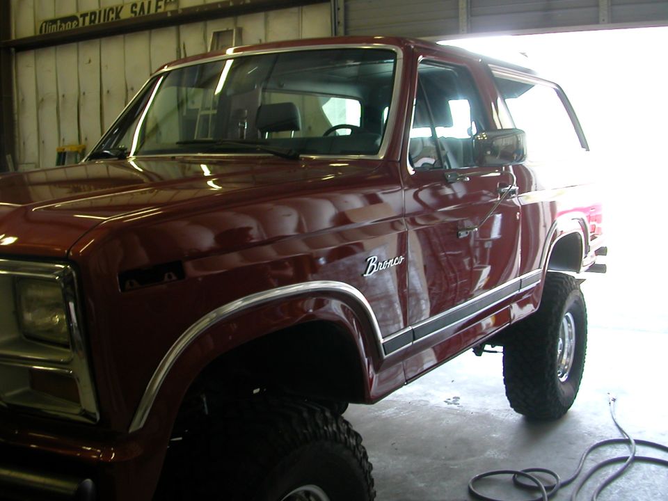 Burgundy Ford Bronco with Bronco script and chrome trim, lifted on mud tires in shop