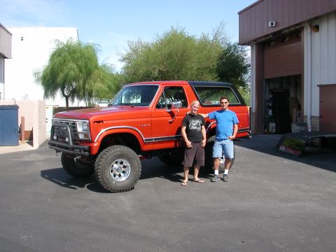 1984 Ford Bronco - Orange Ford Bronco parked outside a garage with two men standing next to it.