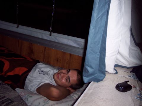 2001 Ford Crown Victoria - A man rests comfortably on a bed, partially covered by a blanket, with curtains visible in the background.