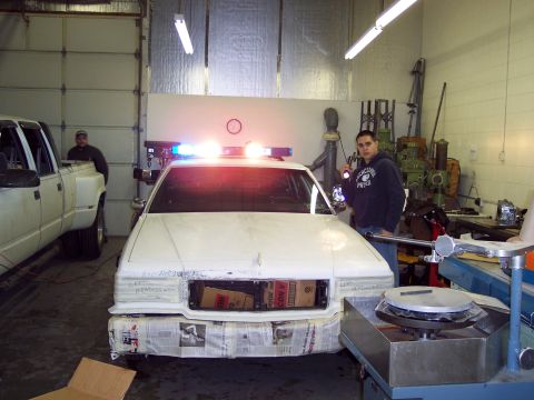 2001 Ford Crown Victoria - A white 2001 Ford Crown Victoria police car is parked in a garage with its emergency lights activated.