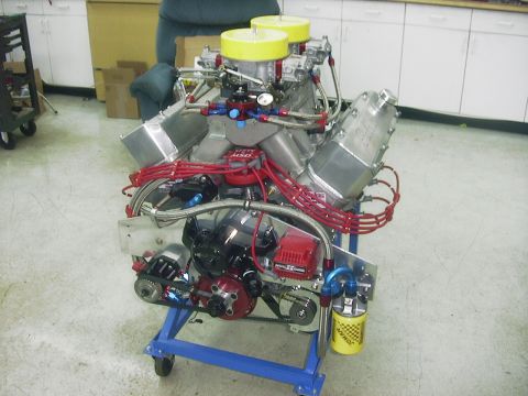 1990 Ford Mustang - A custom V8 engine assembly sits on a blue stand, prominent dual carburetors and red spark plug wires.