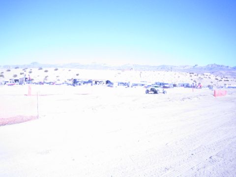 1990 Ford Bronco - small off-road race buggy runs a sandy desert course with orange fencing and a distant pit row behind.