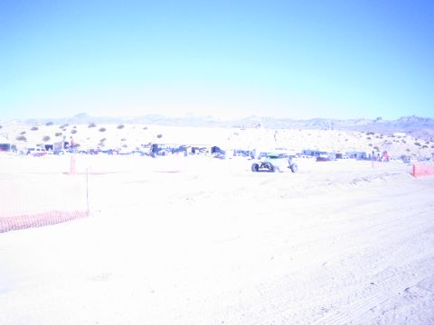 1990 Ford Bronco - small off-road race buggy crosses a washed-out sandy desert course with distant pit vehicles and hills.