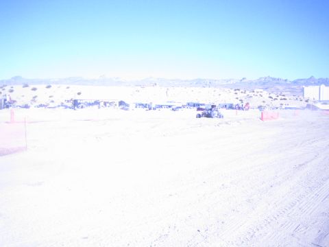 1990 Ford Bronco - bright wide view of a sandy desert off-road race venue with vehicles clustered near the distant pits and mountains.