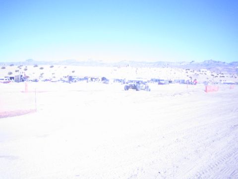 1990 Ford Bronco - off-road buggy sits on an open dirt course in a bright desert basin with a row of pit canopies behind it.