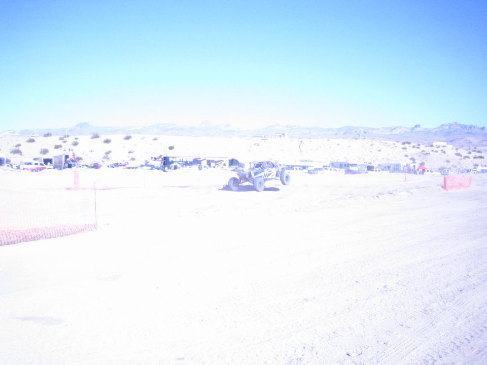 Off-road race car with light-colored body on a desert track near a pit row