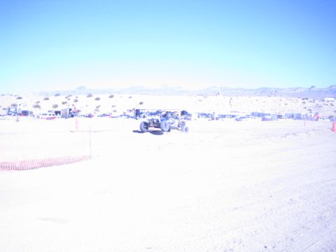 1990 Ford Bronco - tube-chassis off-road buggy crosses a wide sandy desert course backed by distant mountains and pits.