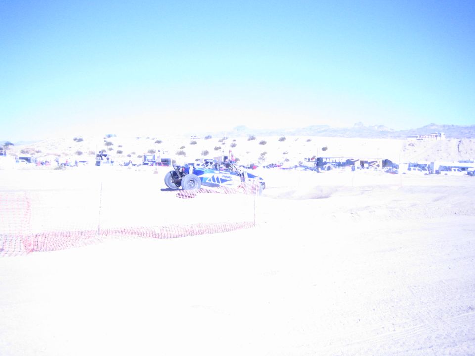 Blue off-road buggy on a desert course behind orange safety fencing