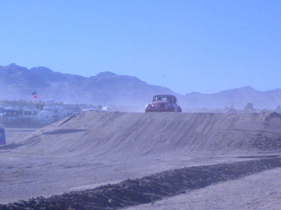 Dark Baja-style VW Beetle racer atop a dirt berm in a dusty desert valley