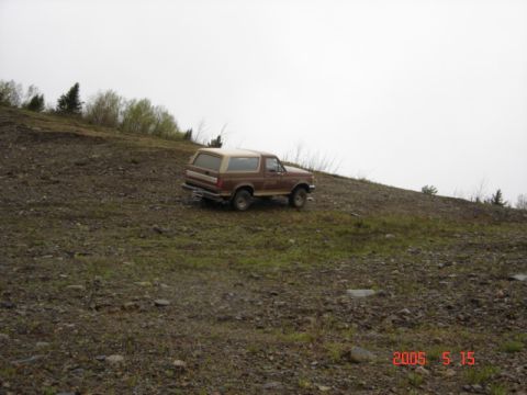 1990 Ford Bronco - Brown 1990 Ford Bronco positioned on a hillside with a cloudy sky overhead.